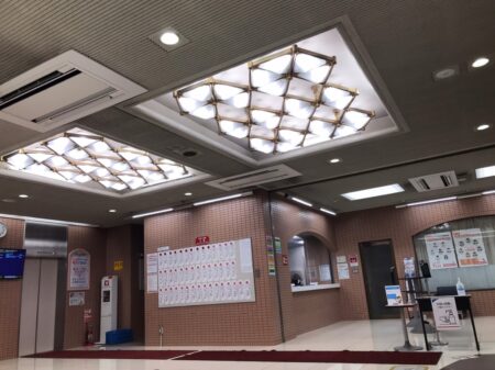 名古屋の学校施設ロビー内部、天井照明と案内窓口のあるエントランスの写真。