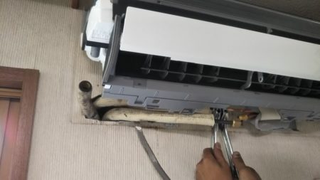 壁掛形ルームエアコンの取付作業中、作業員が工具を使って設置している様子