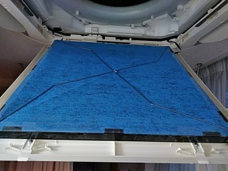 名古屋市の医院でのエアコン洗浄作業中、青いチタンアパタイトフィルターを取り付ける様子