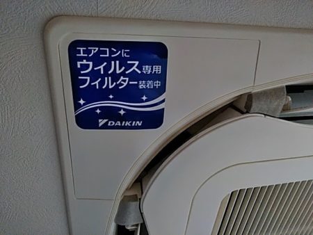 エアコン外部ユニットにウイルス対策フィルター取付を示すラベルが貼られている様子