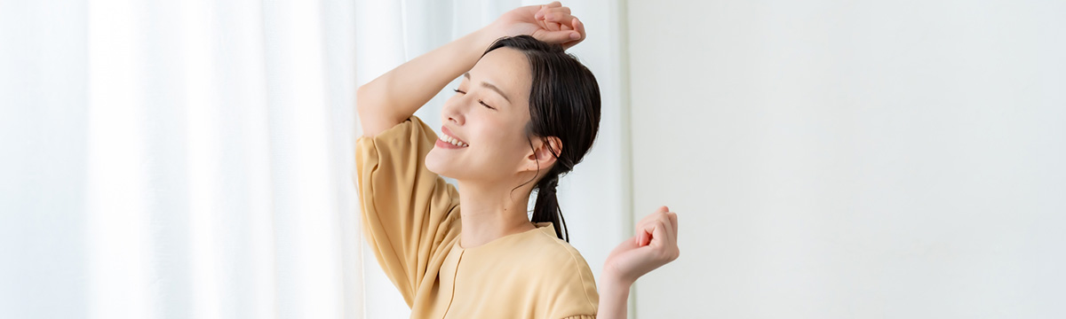 窓際のカーテンの前でリラックスして笑顔を見せる女性の姿